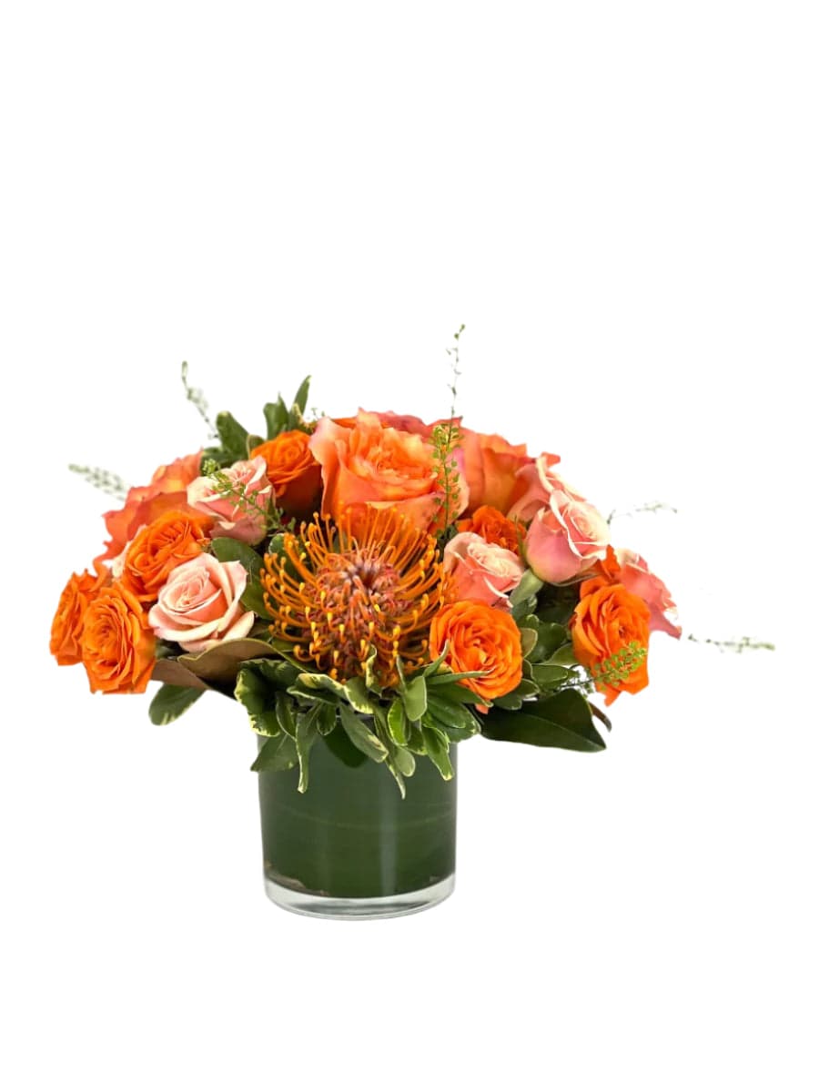Vibrant floral arrangement featuring orange roses and a striking protea in a sleek glass vase.