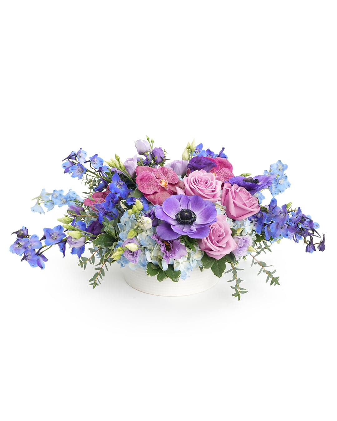 A vibrant floral arrangement featuring purple roses, orchids, and delphiniums in a stylish white vase.