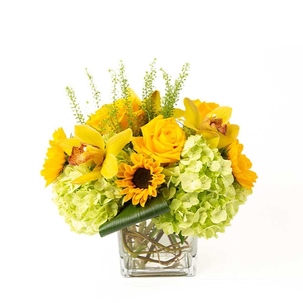Bright floral arrangement featuring yellow roses, sunflowers, and green hydrangeas in a clear glass vase.